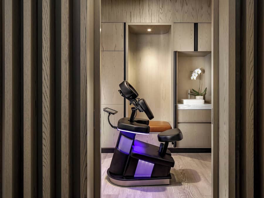 Una moderna silla dental con reposapiés y pedal, ubicada en una habitación con paneles de madera y un estante pequeño con una planta en maceta.