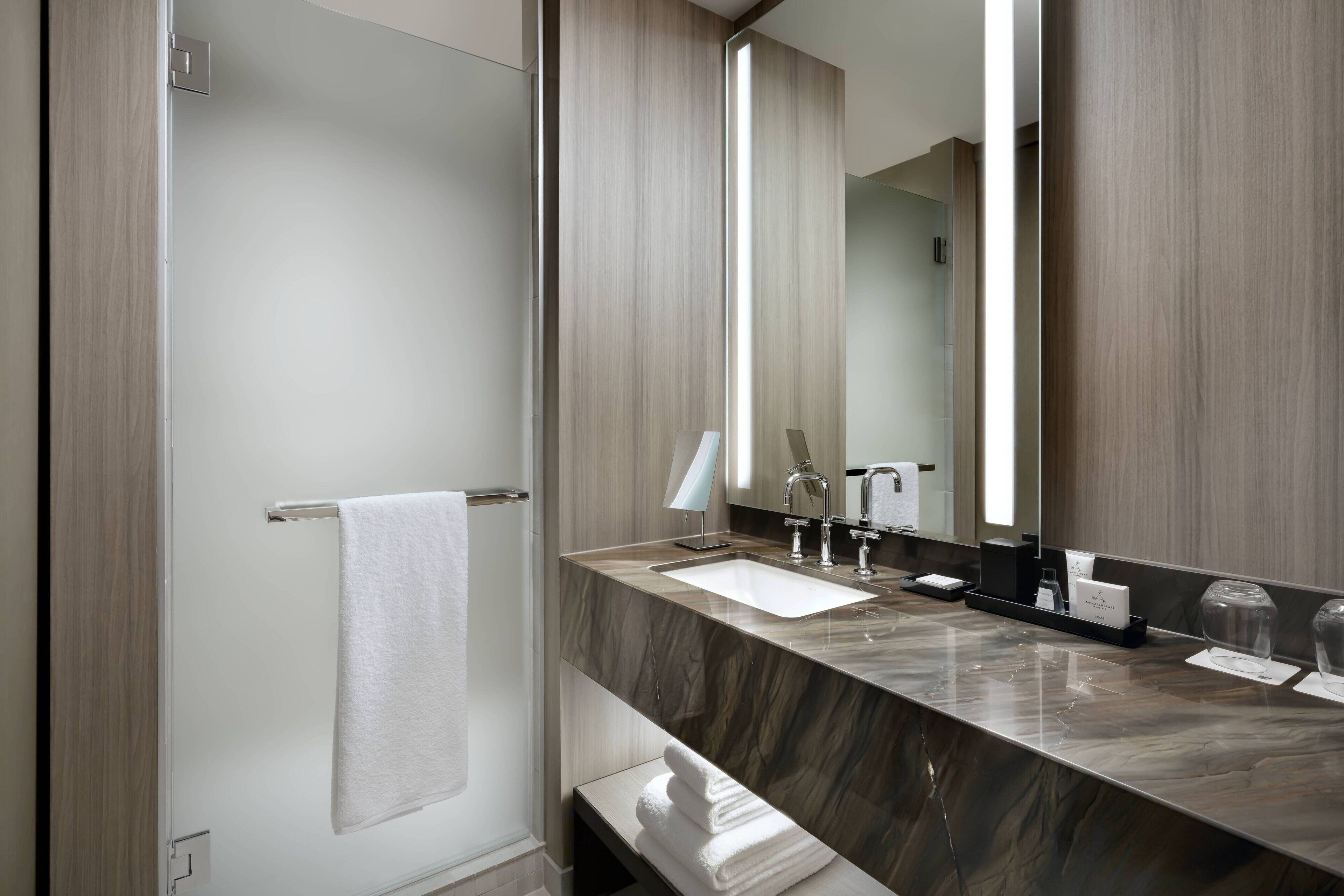 A modern bathroom with a marble countertop, a large mirror, and a towel rack.