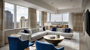 A modern living room with a sectional sofa, blue armchairs, a coffee table, and a city view through large windows. - JW Marriott Edmonton ICE District (Edmonton)