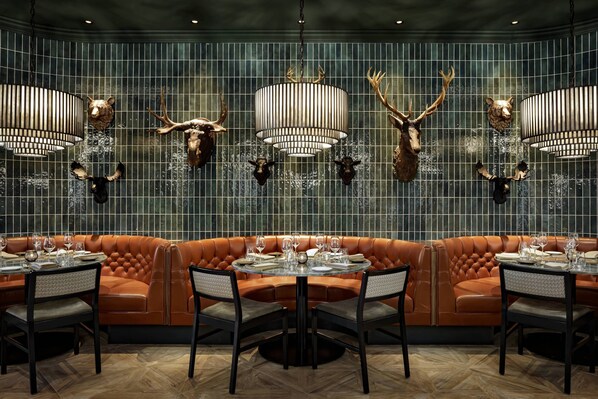 A restaurant with a leather booth seating area, round tables, and chandeliers with antler decorations. - JW Marriott Edmonton ICE District (Edmonton)