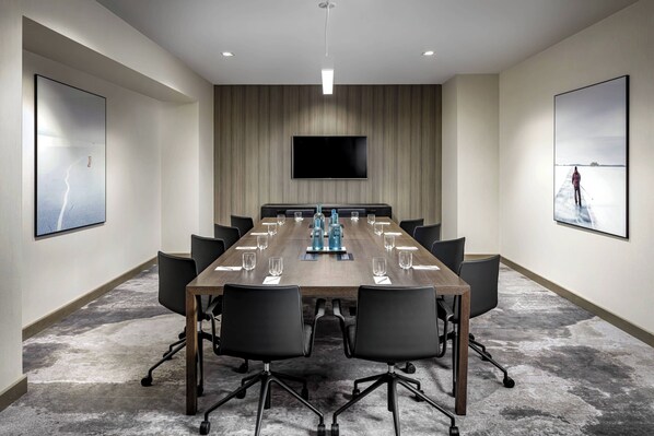 Un salón de conferencias con una larga mesa, sillas, un televisor de pantalla plana y obras de arte en las paredes.