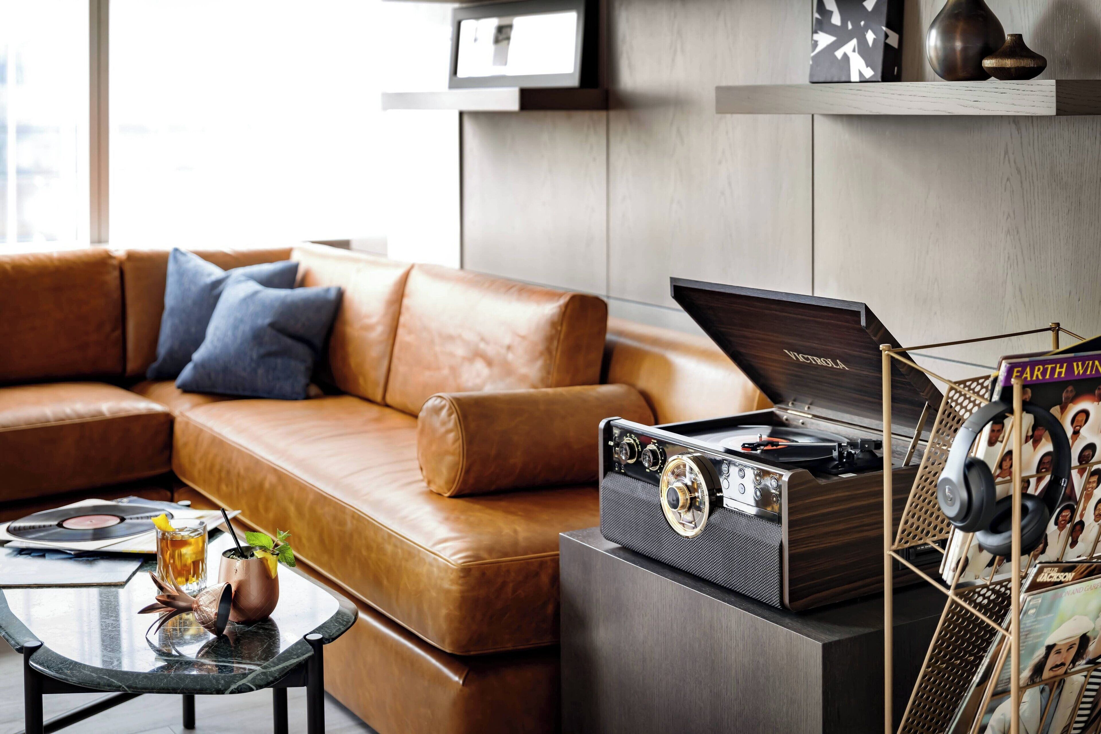A modern living room with a leather sofa, a glass coffee table with a drink and a plant, and a vintage turntable on a cabinet.
