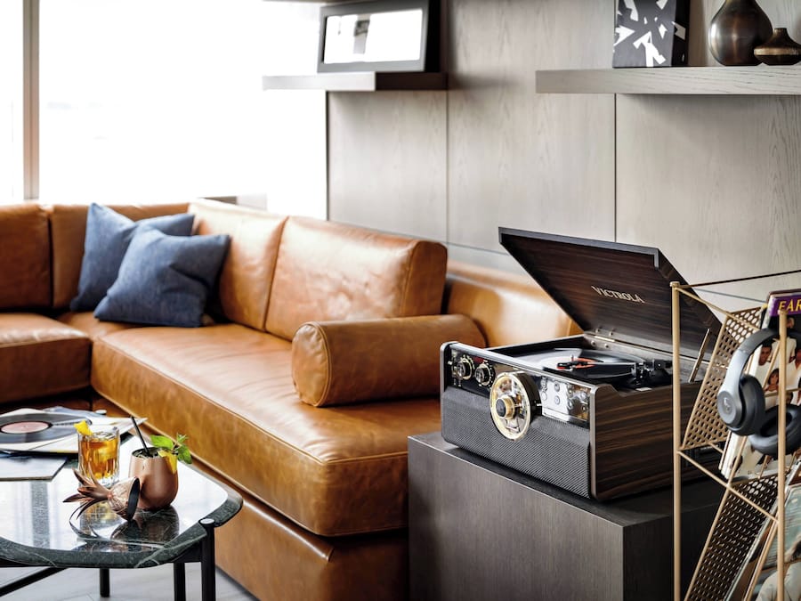 A modern living room with a leather sofa, a glass coffee table with a drink and a plant, and a vintage turntable on a cabinet.