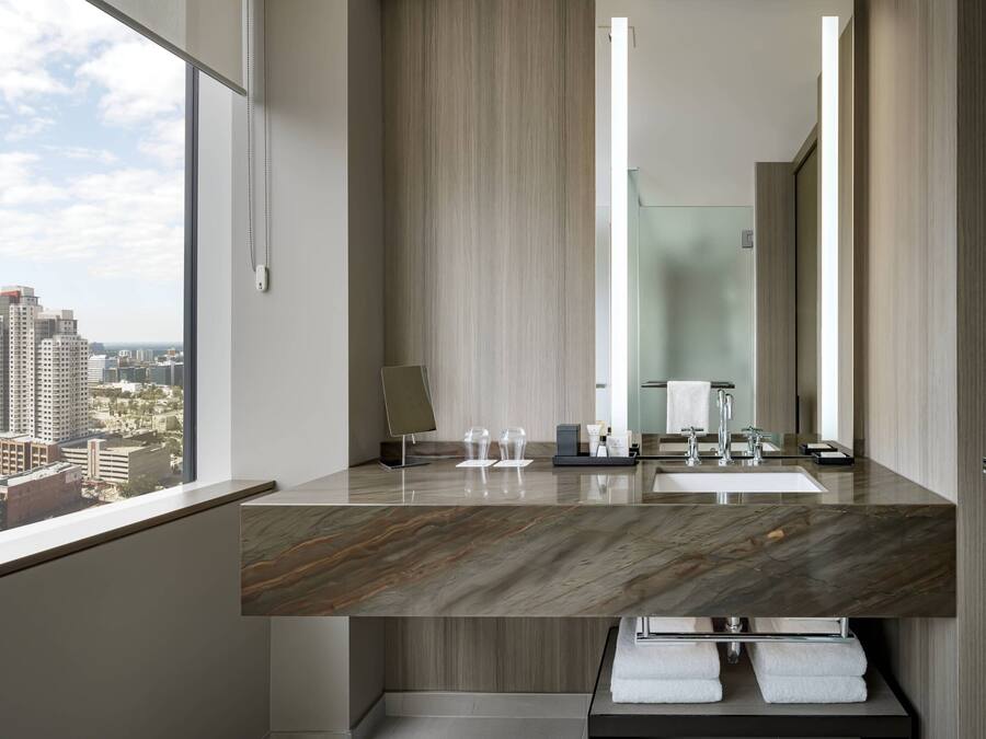 Un baño moderno con encimera de mármol, un espejo grande y vistas de la ciudad a través de la ventana.