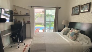 A bedroom with a bed, a desk, a chair, a TV, and a view of a pool. - YurInn (Cancun)