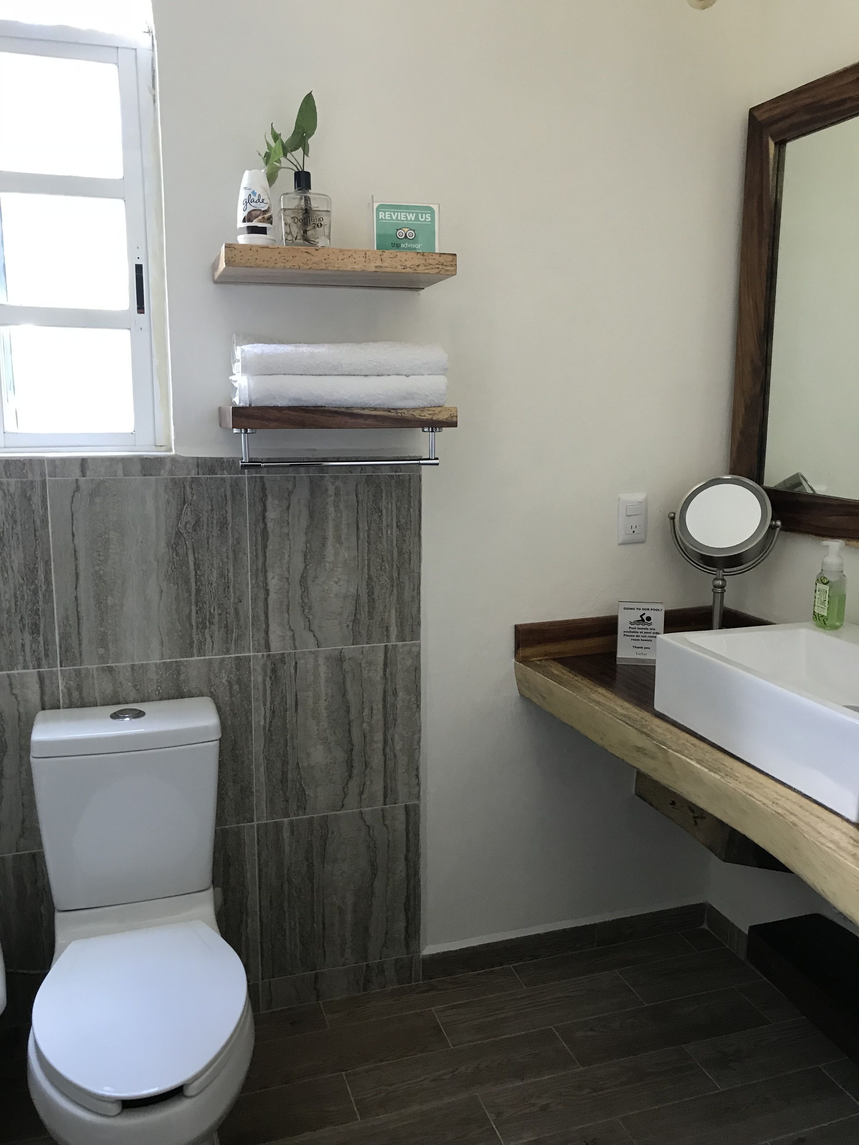A bathroom with a toilet, a sink with a mirror, a towel rack, and a sign that says "REVIEW US".
