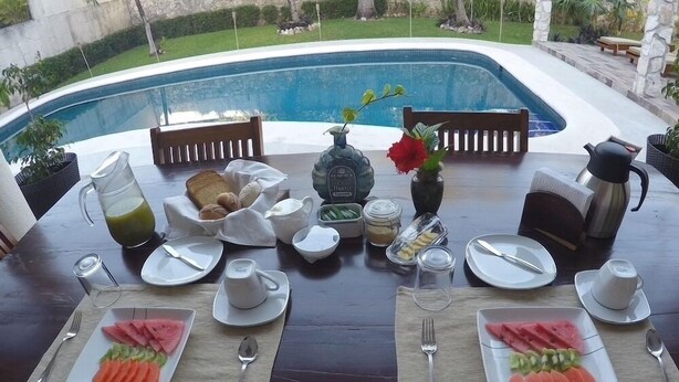 Une table à manger dressée avec des aliments pour le petit-déjeuner, donnant sur une piscine.