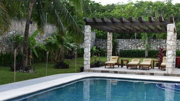 A swimming pool with a stone wall and a pergola with chairs. - YurInn (Cancun)