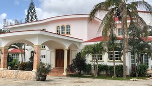 A large, two-story building with a red roof and white walls, featuring a covered entrance with arches and a large potted plant. - YurInn (Cancun)