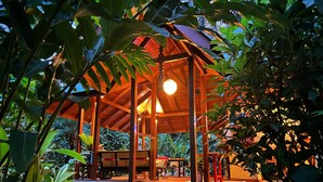 A wooden gazebo with a bench, surrounded by dense foliage.