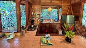 A wooden kitchen with a gas stove, sink, and a refrigerator. There is a window with a view of greenery outside.