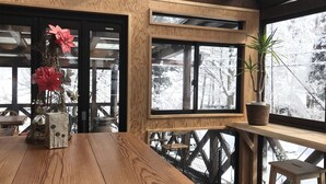 A wooden table with a vase of red flowers and a potted plant on a window sill. - ALP Lodge (Hakuba)