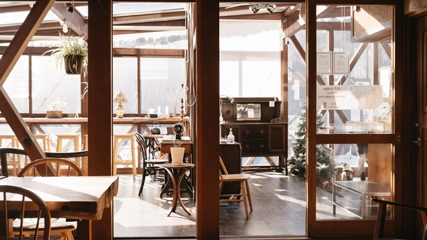 A wooden interior with a dining area, a kitchen, and a view through a glass door. - ALP Lodge (Hakuba)