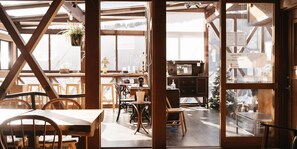 A wooden interior with a dining area, a kitchen, and a view through a glass door. - ALP Lodge (Hakuba)