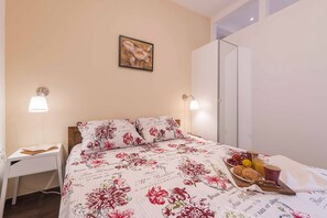 A neatly made bed with floral bedding, a bedside table with a lamp, and a tray with breakfast items. - Great location for a great vacation! (Pula)