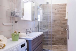 A modern bathroom with a glass shower enclosure, a white sink, and a built-in washing machine. - Great location for a great vacation! (Pula)