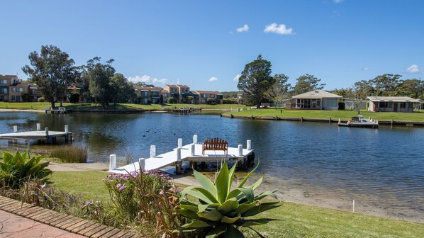 A lakeside view with a dock, a bench, and a grassy area with plants.