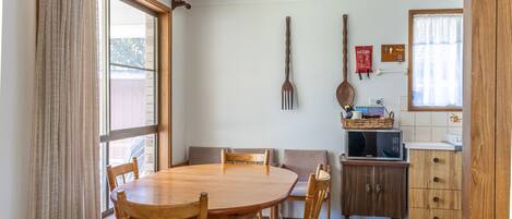 A dining area with a wooden table and chairs, a microwave on a cabinet, and a window with curtains.
