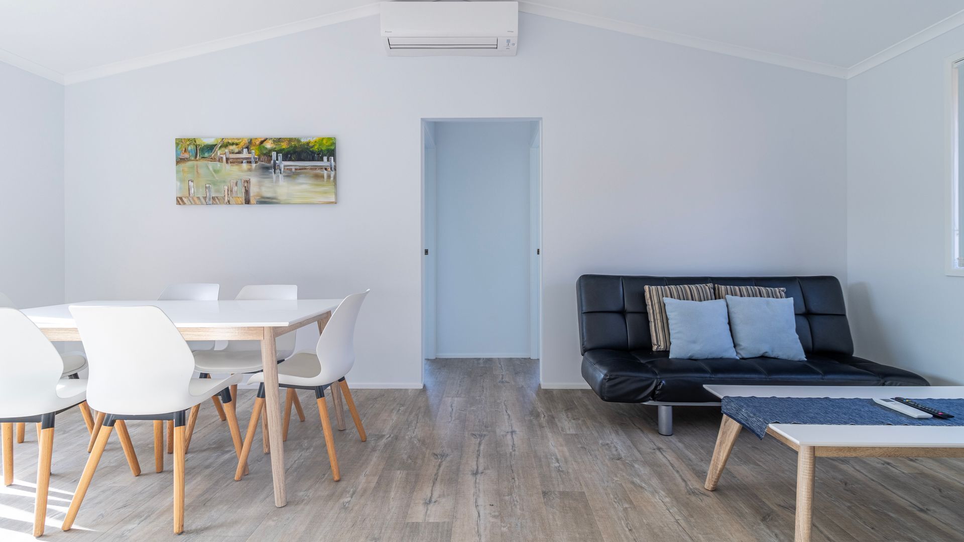 Een moderne woonkamer met een eethoek, een zwarte leren bank en een schilderij aan de muur.