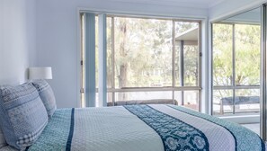 Relax in this serene bedroom with a large bed and sliding glass door leading to a tranquil outdoor space.