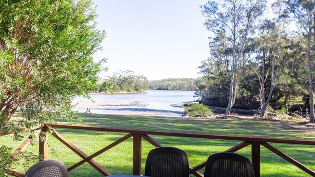 Une terrasse avec vue sur un lac, entourée d’arbres et d’une zone herbeuse.