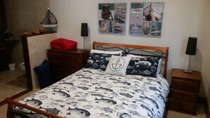 A bedroom with a bed featuring a fish pattern bedspread, a wooden headboard, and a nightstand with a lamp.