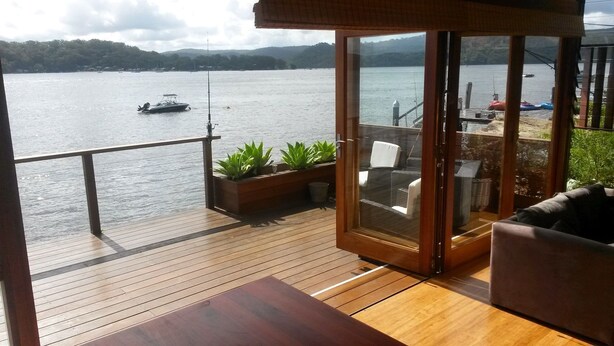 A wooden deck with a glass door leading to a seating area with a view of a lake and a boat.