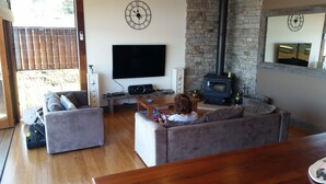 A living room with a sofa, a coffee table, a TV, and a stone wall with a fireplace.