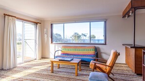 A room with a large window, a sofa, a chair, a table, and a cabinet. - Berrara Cove Beach House (Berrara)