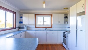 A modern kitchen with white cabinets, a microwave, a sink, and a window. - Berrara Cove Beach House (Berrara)