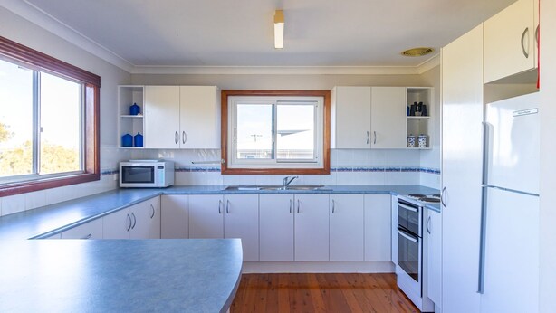 A modern kitchen with white cabinets, a microwave, a sink, and a window. - Berrara Cove Beach House (Berrara)