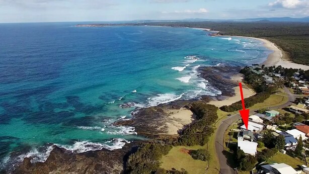 An aerial view of a coastal area with a beach, rocky shoreline, and residential buildings. - Berrara Cove Beach House (Berrara)