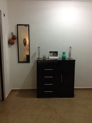 A room with a cabinet and a framed mirror, featuring a vase on top.
