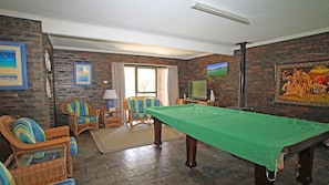 Une pièce équipée d’une table de billard, de fauteuils en osier, d’un téléviseur et d’une cheminée.