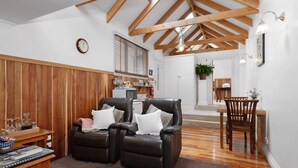 Een woonkamer met een houten plafond, twee leren fauteuils, een houten salontafel, en een eethoek met een houten tafel en stoelen.