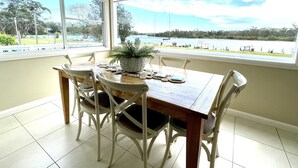 A dining area with a table and chairs, a potted plant, and a view of a lake and boats. - Riverbank Cottage - Waterfront (Sussex Inlet)