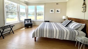 A bedroom with a large bed, a ceiling fan, a chair, and a small table. - Riverbank Cottage - Waterfront (Sussex Inlet)