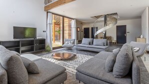 Una sala de estar moderna con televisor, sofás grises, una mesa de centro y una escalera espiral.