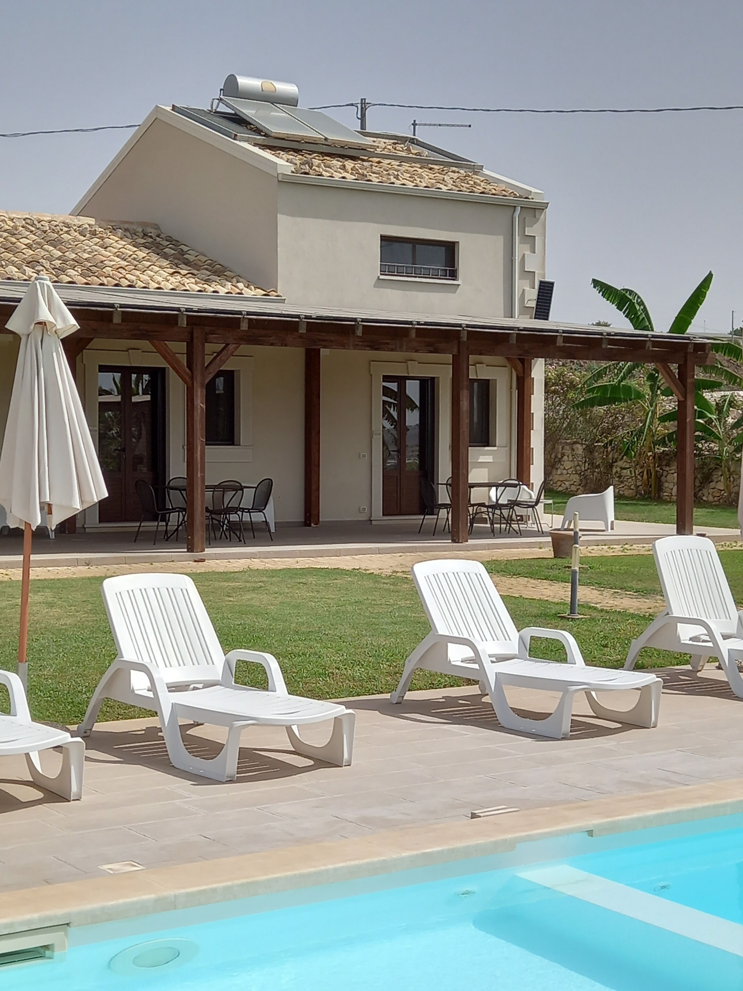 Una casa amb piscina, gandules blanques i una zona de pati coberta.