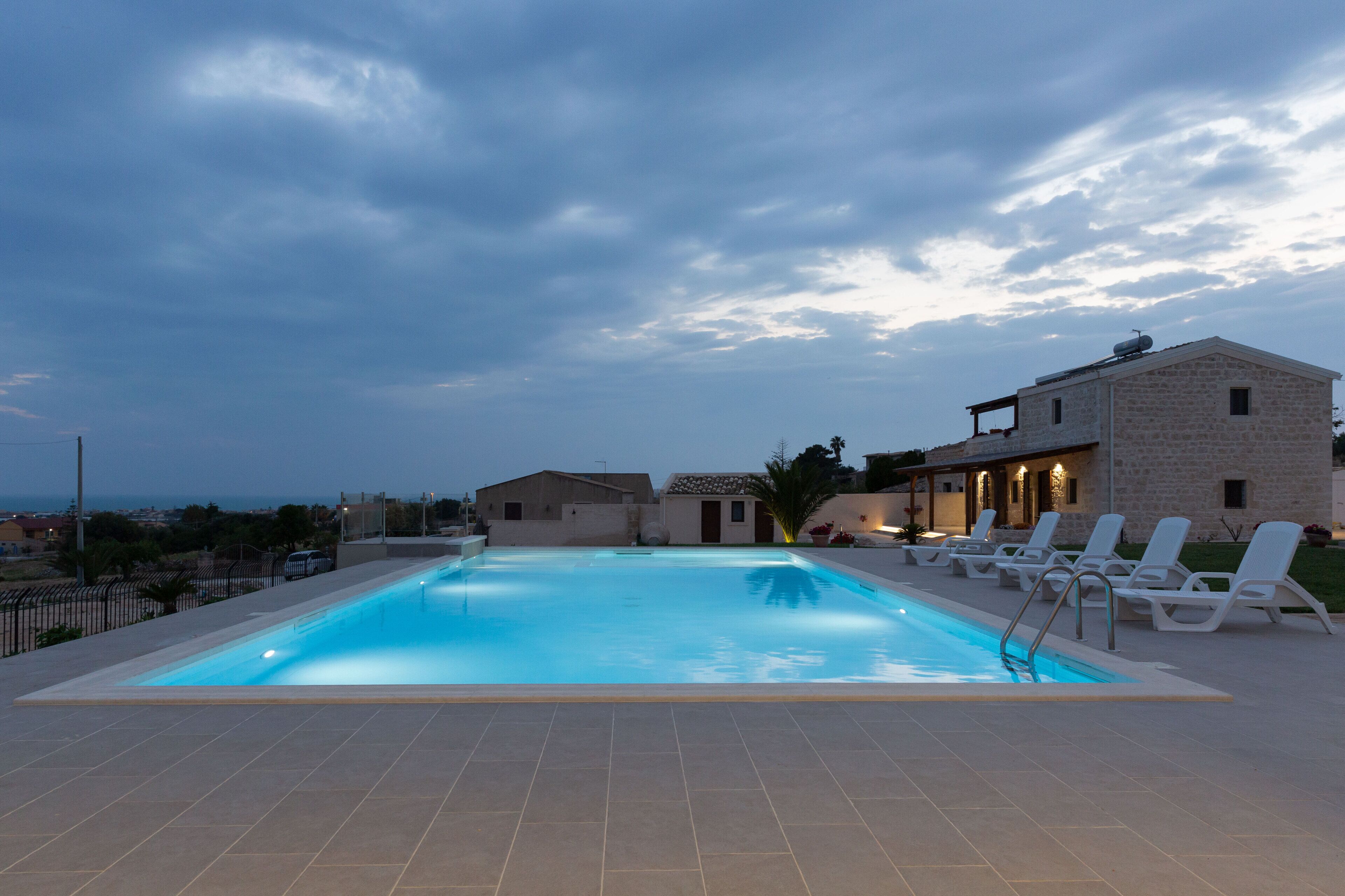 Una piscina con sillas de descanso, un edificio de piedra y vistas al mar.