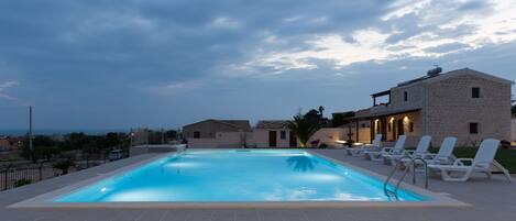 Una piscina con sillas de descanso, un edificio de piedra y vistas al mar.