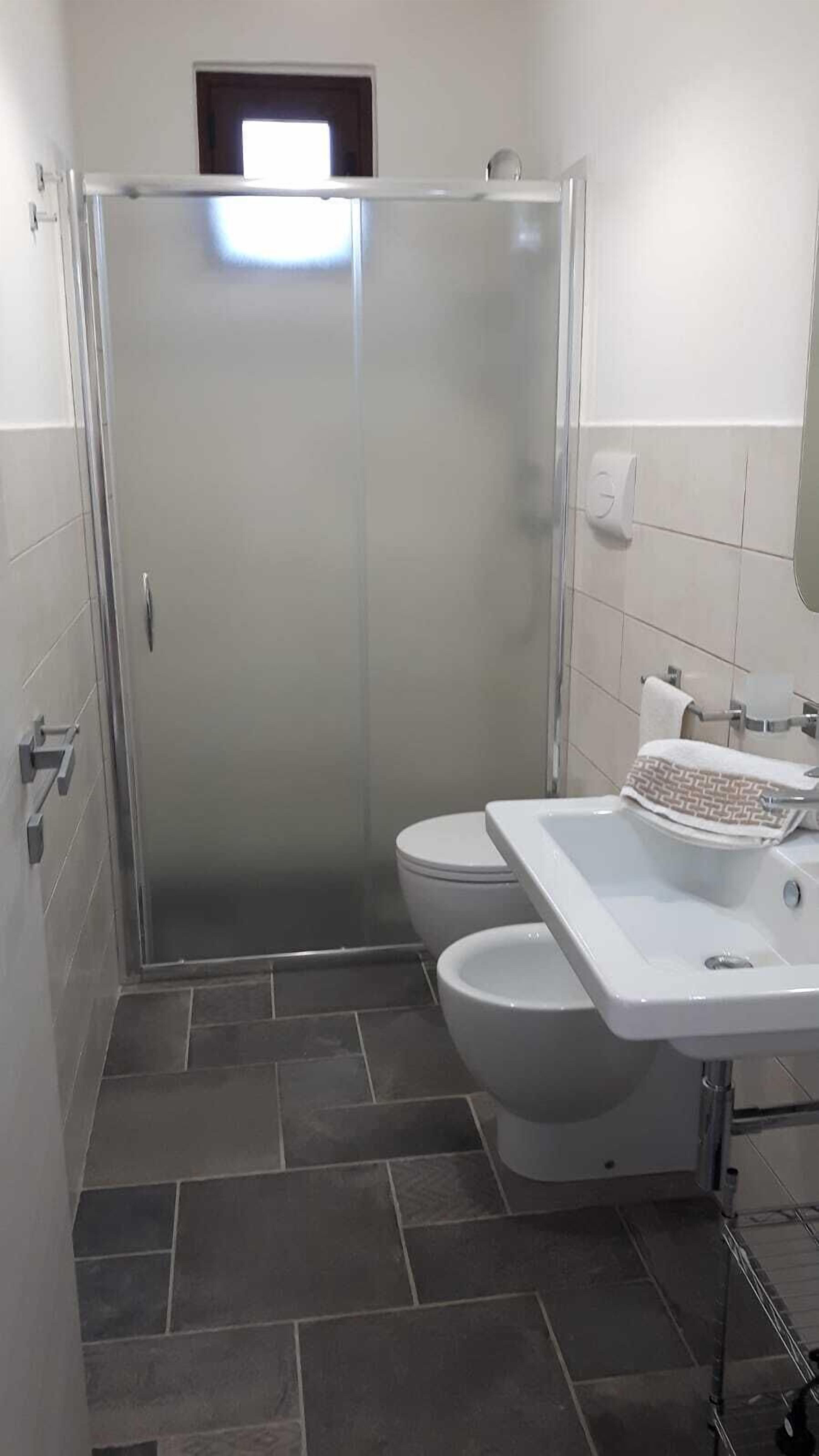 A bathroom with a glass shower enclosure, a toilet, and a sink with a towel.