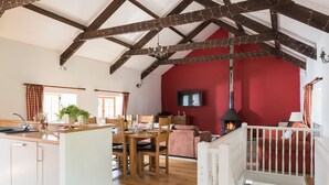 A spacious living area with a high ceiling, wooden beams, a fireplace, a dining table with chairs, and a cozy seating area. - Kingfisher Barn, stunning location, private hot tub, tennis, river frontage (Saltash)