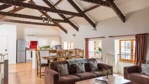 A spacious living area with a brown sofa, wooden coffee table, and a dining area with wooden chairs and a red tablecloth. - Kingfisher Barn, stunning location, private hot tub, tennis, river frontage (Saltash)