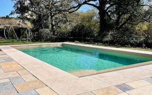 A rectangular swimming pool with clear water, surrounded by a stone deck.