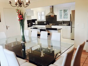 A modern kitchen with white cabinets, a black countertop, and a dining area with a glass table and white chairs. - Large Family Villa, Les Issambres private pool, gorgeous sea views, 5 bedrooms (Roquebrune-sur-Argens)