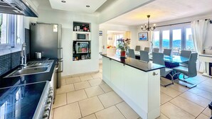 A modern kitchen with a central island, built-in appliances, and a dining area with a view. - Large Family Villa, Les Issambres private pool, gorgeous sea views, 5 bedrooms (Roquebrune-sur-Argens)