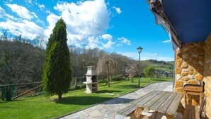 Un patio in pietra con tavolo e panche in legno, un muro di pietra e vista su una zona erbosa con alberi e una struttura in pietra.
