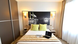A hotel room with a bed, a laptop, a night view poster, and a lamp. - Studio confort proche du centre + Wi-Fi gratuit (Bordeaux)