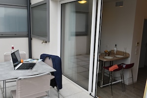 Ein modernes Zimmer mit Glastür zu einem Essbereich, einem Laptop auf einem Tisch und einem Stuhl mit einer Jacke.